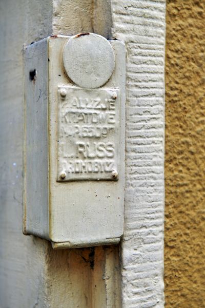 Informacja o producencie żaluzji kratowych wyprodukowanych w fabryce w Drohobyczu, umieszczona na ramie kraty w kamienicy przy ul. Grunwaldzkiej 6. Po reorganizacji w 1936 roku Towarzystwa Muzeum Przemysłowego na Związek Popierania Wytw&oacute;rczości Ziemi Rzeszowskiej,  jedną z gł&oacute;wnych form działalności tej instytucji była organizacja konkurs&oacute;w witryn sklepowych. Aktywność na tym polu, mająca na celu promocję  lokalnych wyrob&oacute;w jako przejawu siły odradzającego się z niewoli państwa, przyczyniła się także niewątpliwie do podniesienia konkurencji oraz jakości prezentowanych towar&oacute;w sklepowych, a także estetyki aranżacji witryn. Fot. Bogdan Szczupaj, Pola Antonina Słomińska, Galeria Fotografii Miasta Rzeszowa